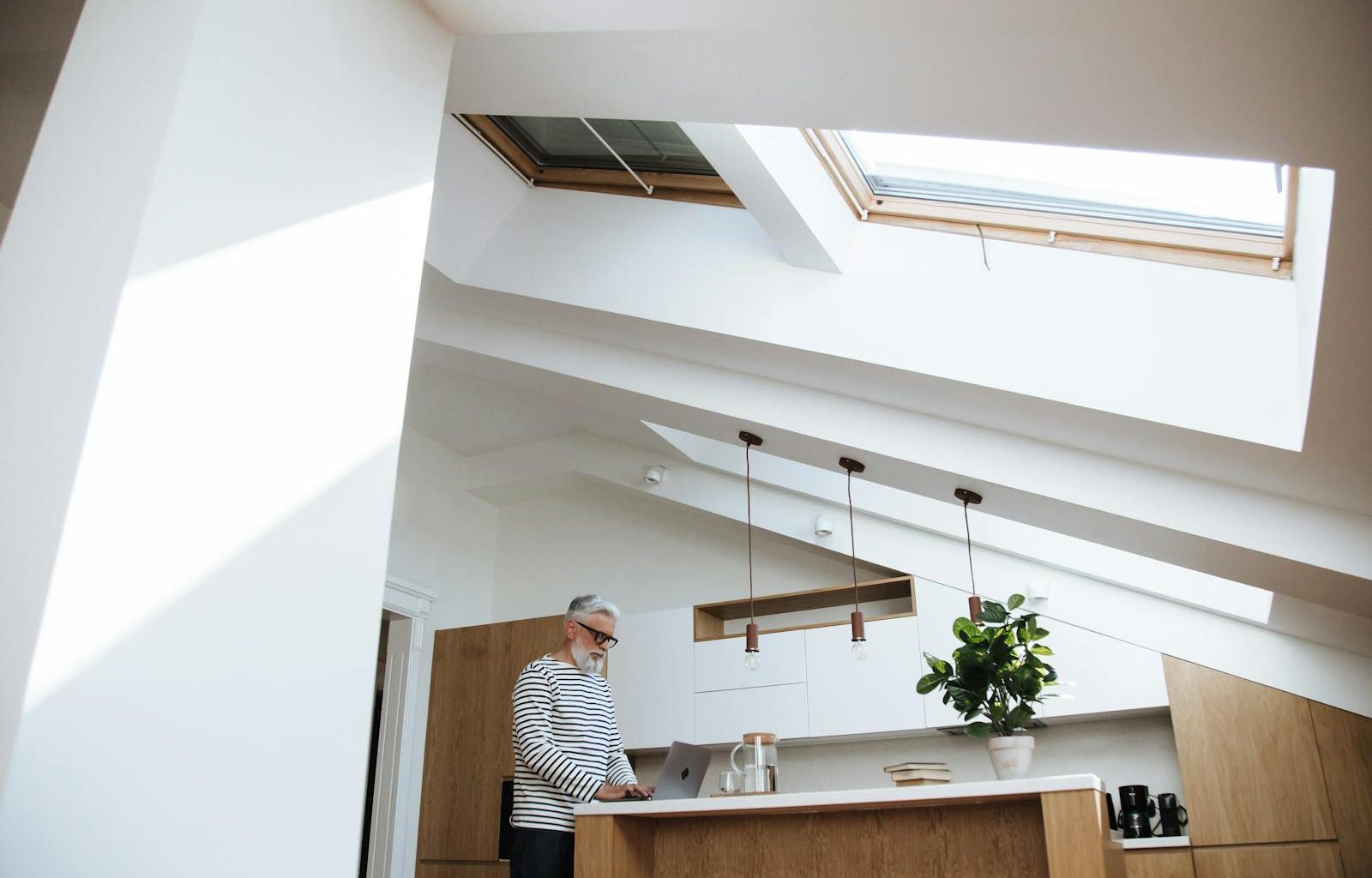 Gray-haired man at home office using laptop in bright kitchen space.