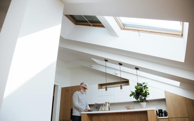Gray-haired man at home office using laptop in bright kitchen space.