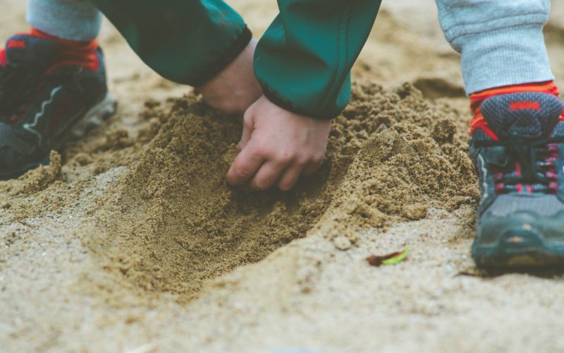 person in blue long sleeve shirt and blue denim jeans standing on brown sand during daytime