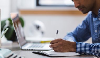 Een jonge atleet zit met een laptop en een sporttas aan een tafel te studeren