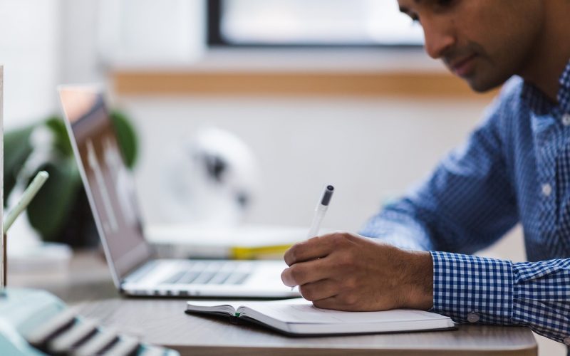 Een jonge atleet zit met een laptop en een sporttas aan een tafel te studeren