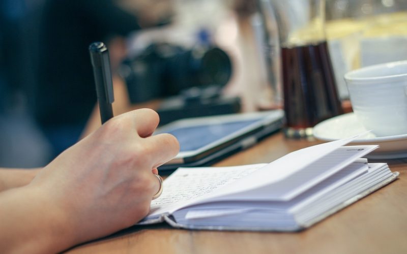 Persoon schrijft een takenlijst aan een bureau om uitstelgedrag aan te pakken