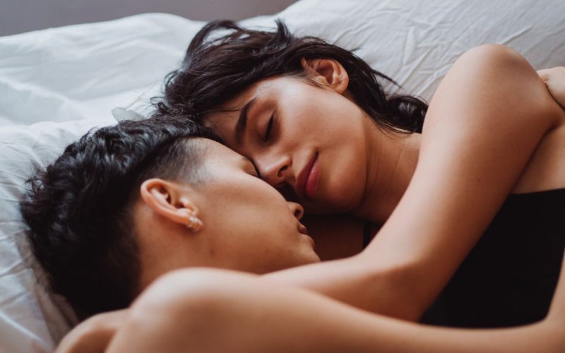 A loving couple sleeps peacefully, embracing each other closely with content expressions.