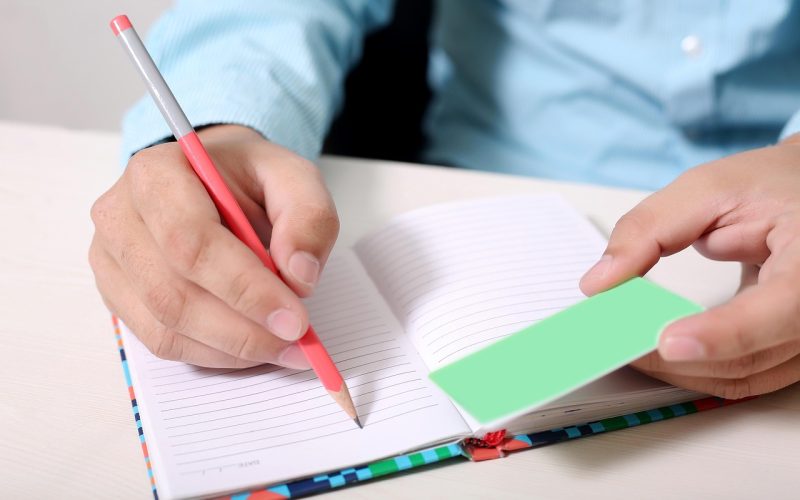 Persoon schrijft aantekeningen in notitieboek aan tafel